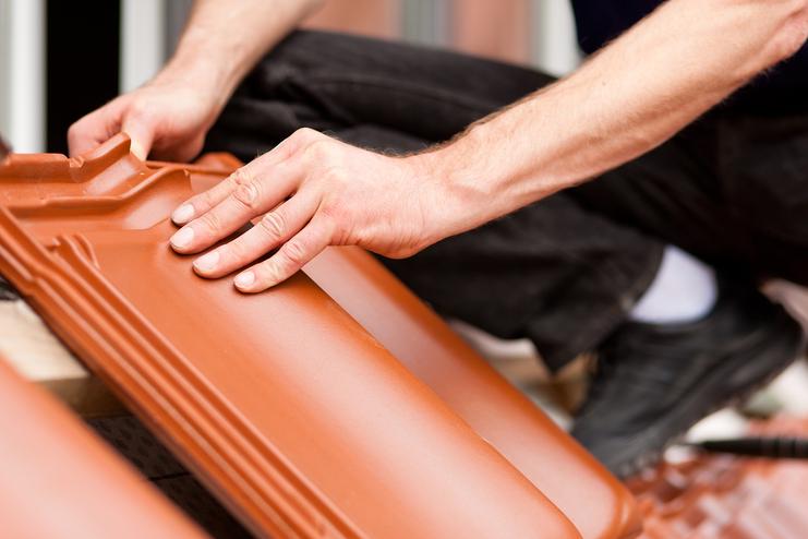 Arbeiter verlegt Dachziegel auf einer Baustelle, Hände drücken einen Ziegel an seinen Platz.