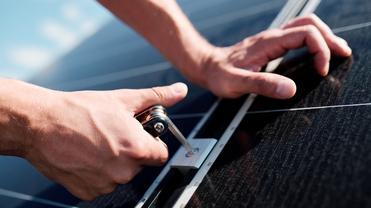 Ein Techniker montiert eine Halterung an einem Solarpanel unter blauem Himmel.