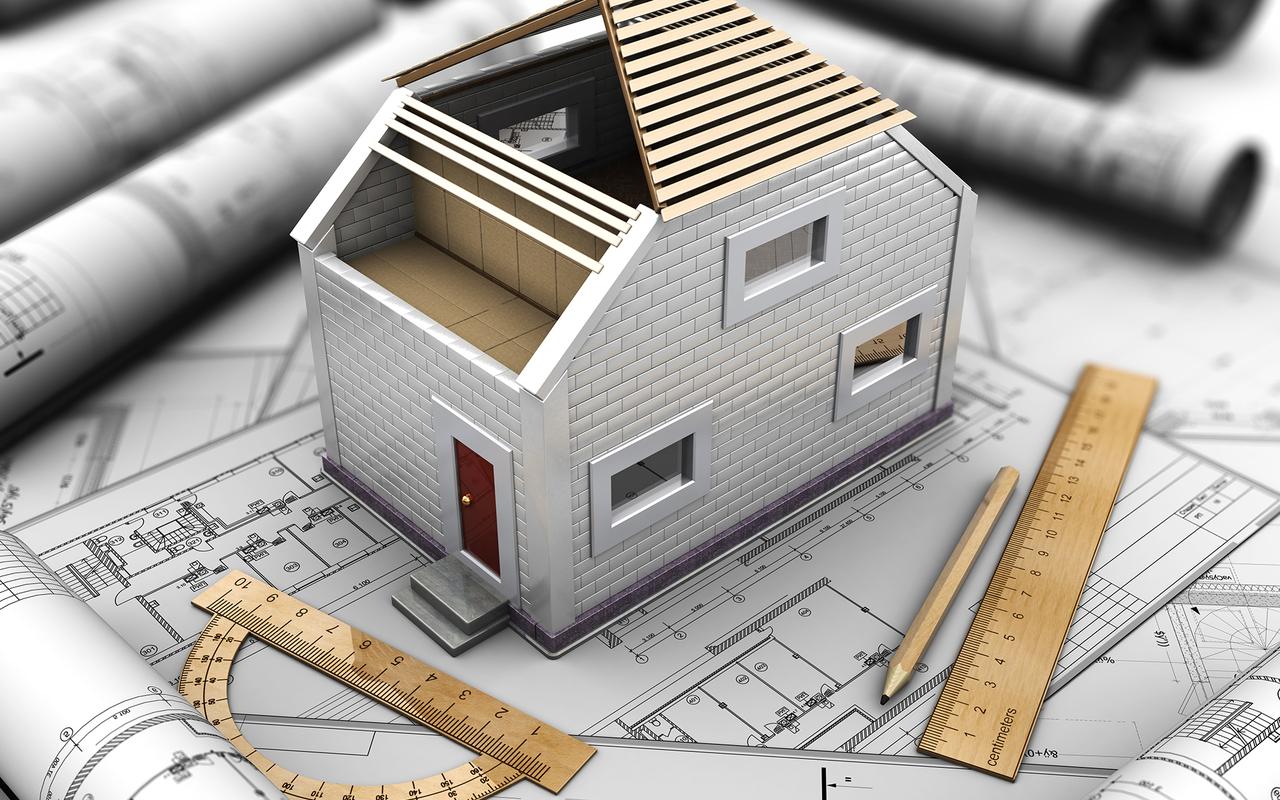 Modell eines Hauses mit offenem Dach auf Bauplänen, dazu Lineal, Winkelmesser und Bleistift auf einem Tisch.